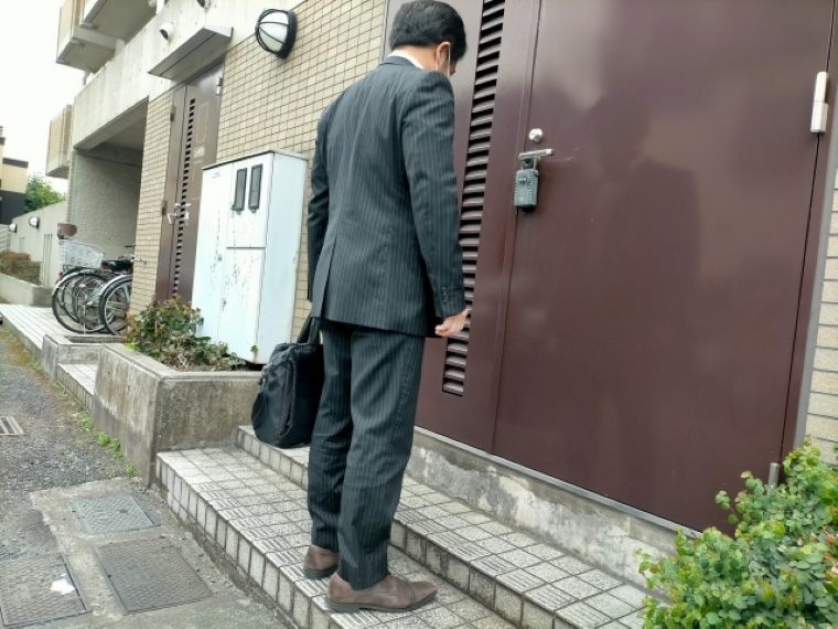 訪問営業で玄関前に立つスーツ姿の男性