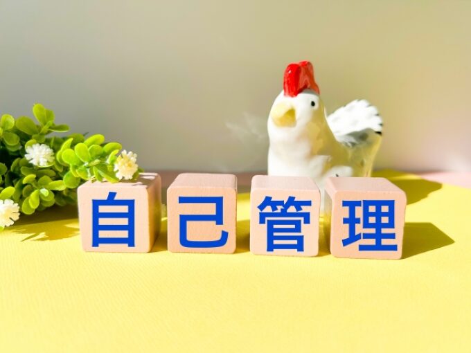 「自己管理」と書かれたブロックと、背景にニワトリの置物と植物があるイメージ