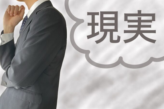 スーツ姿の男性が現実と向き合いながら営業職への転職を考えている様子を表す画像